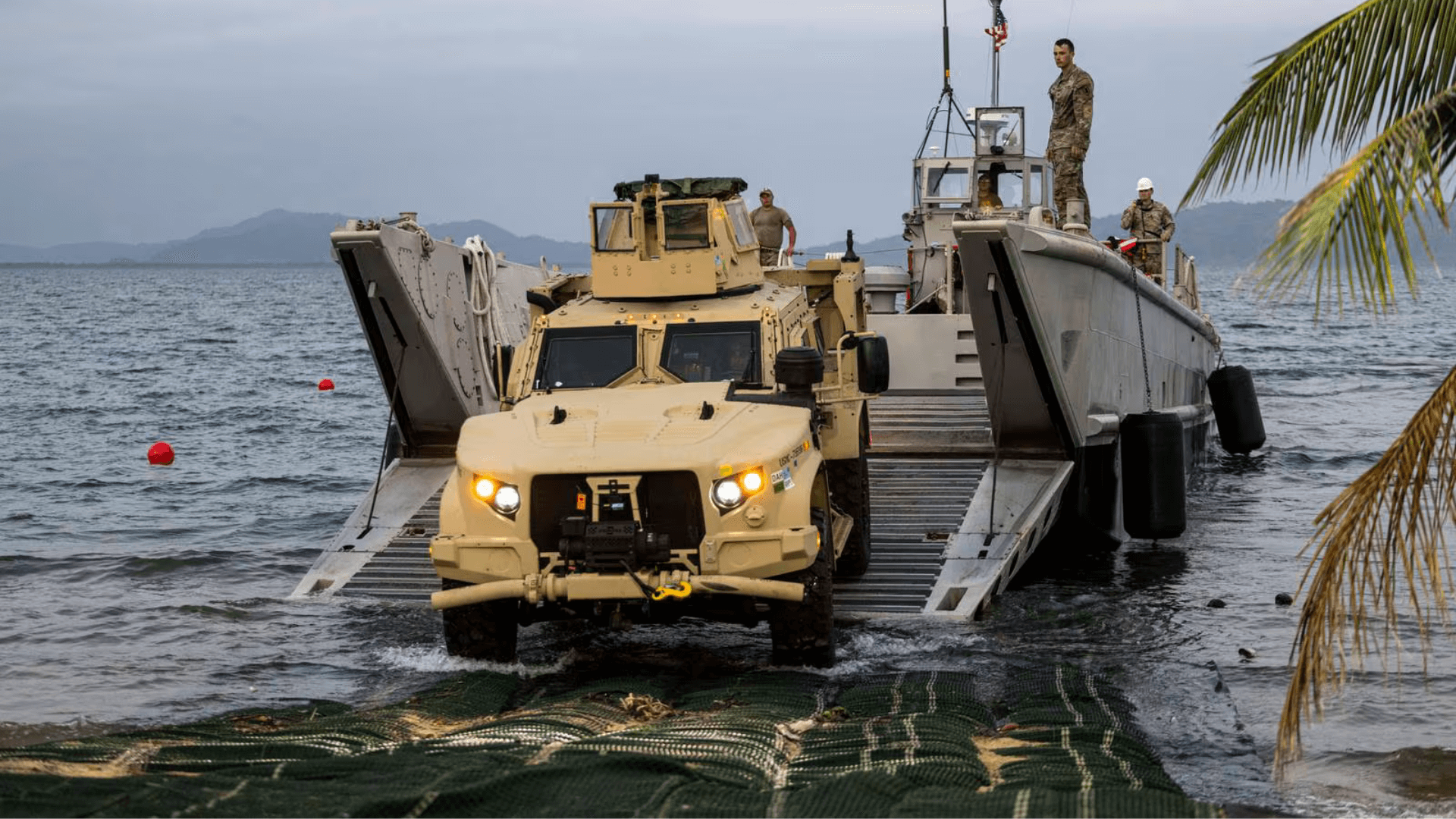 A U.S. Marine drives a Joint Light Tactical Vehicle off an Army landing craft onto SUBMAT during Balikatan 23 at Camp Agnew, Philippines.